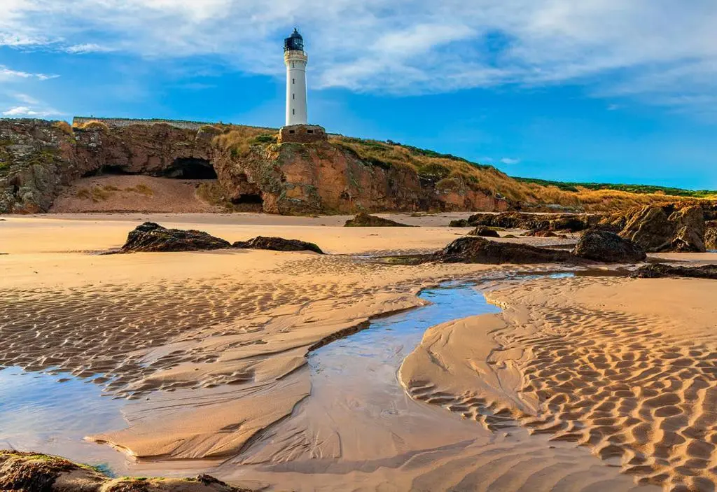 a beach with a lighthouse on top of a hill at Cosy Cottage Close to East Beach, Shops, Restaurants and RAF base in Lossiemouth