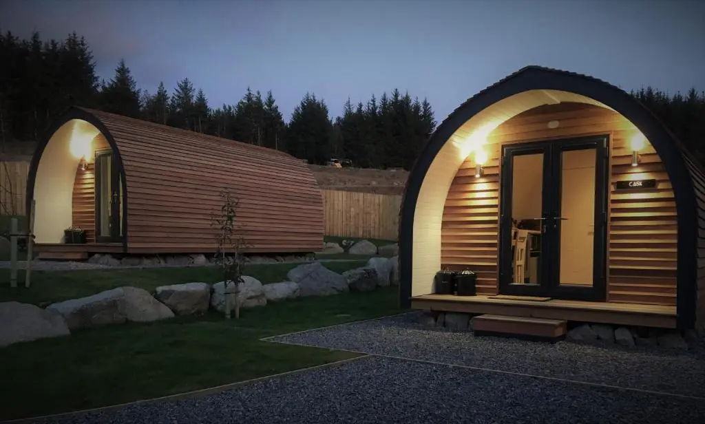 a small wooden cabin in a yard at night at Tomatin Glamping Pods in Inverness