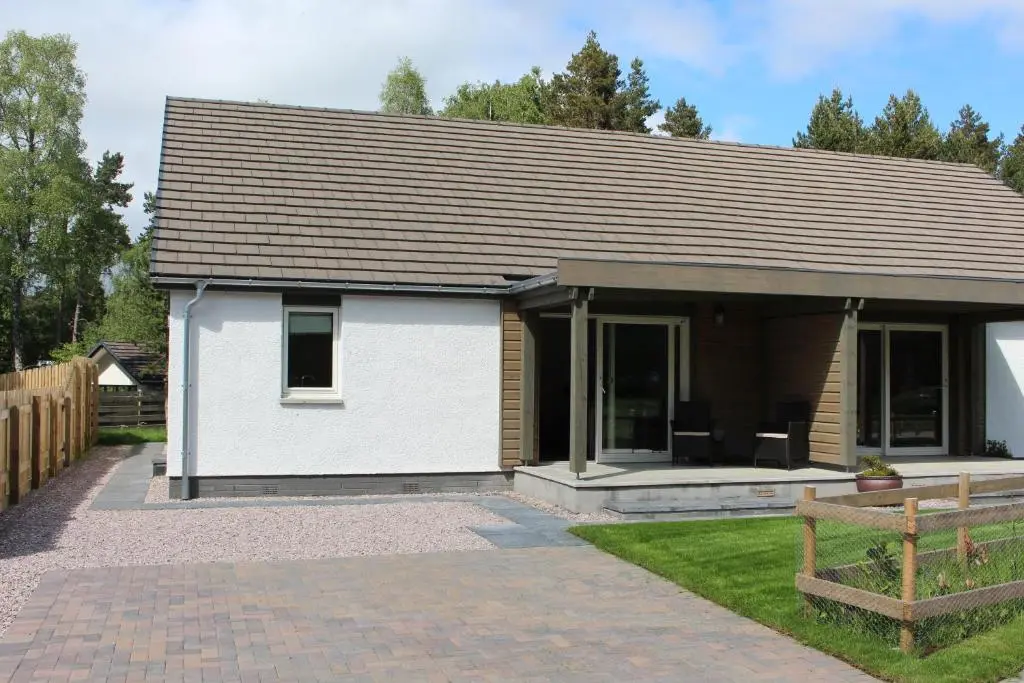 a small white house with a porch and a fence at 2 Dellmhor Cottages in Aviemore