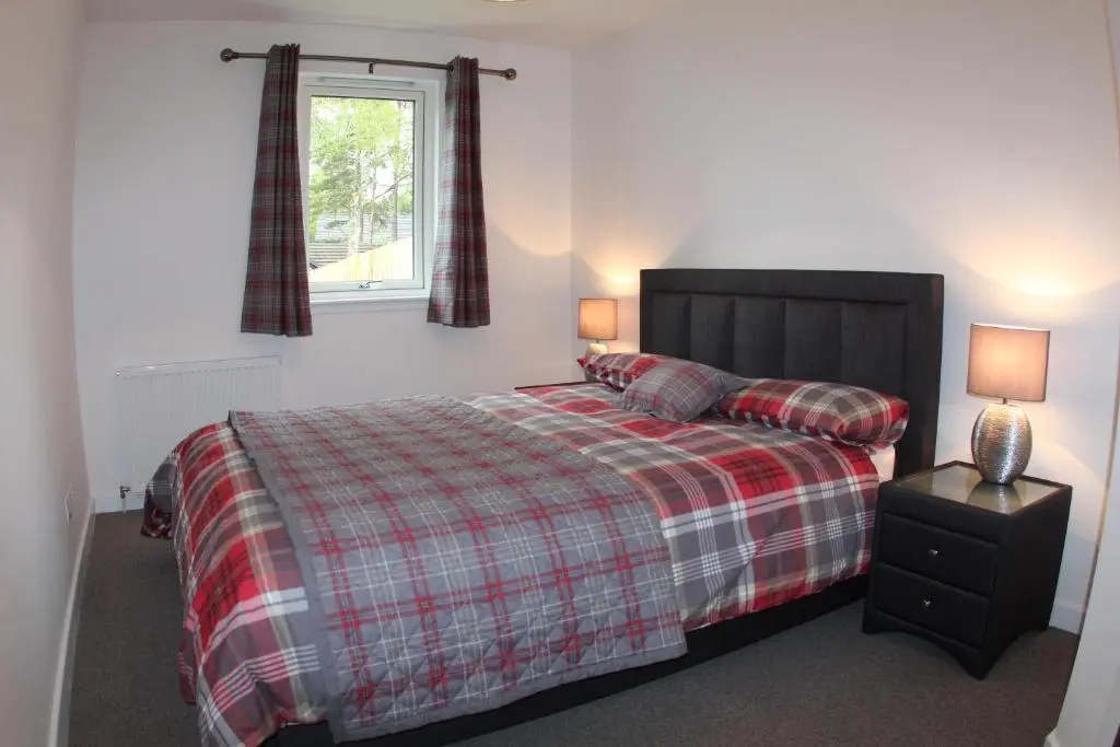 a bedroom with a bed with a plaid blanket and a window at 2 Dellmhor Cottages in Aviemore