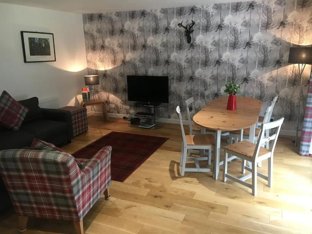 a living room with a table and a tv at 2 Dellmhor Cottages in Aviemore