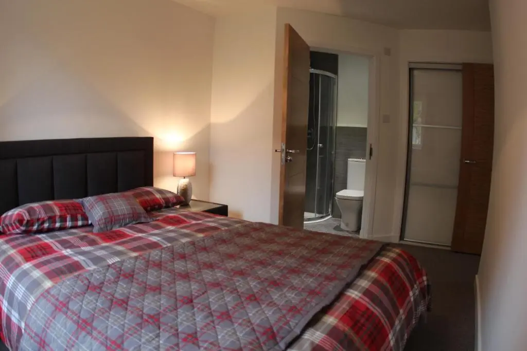a bedroom with a bed and a bathroom with a toilet at 2 Dellmhor Cottages in Aviemore