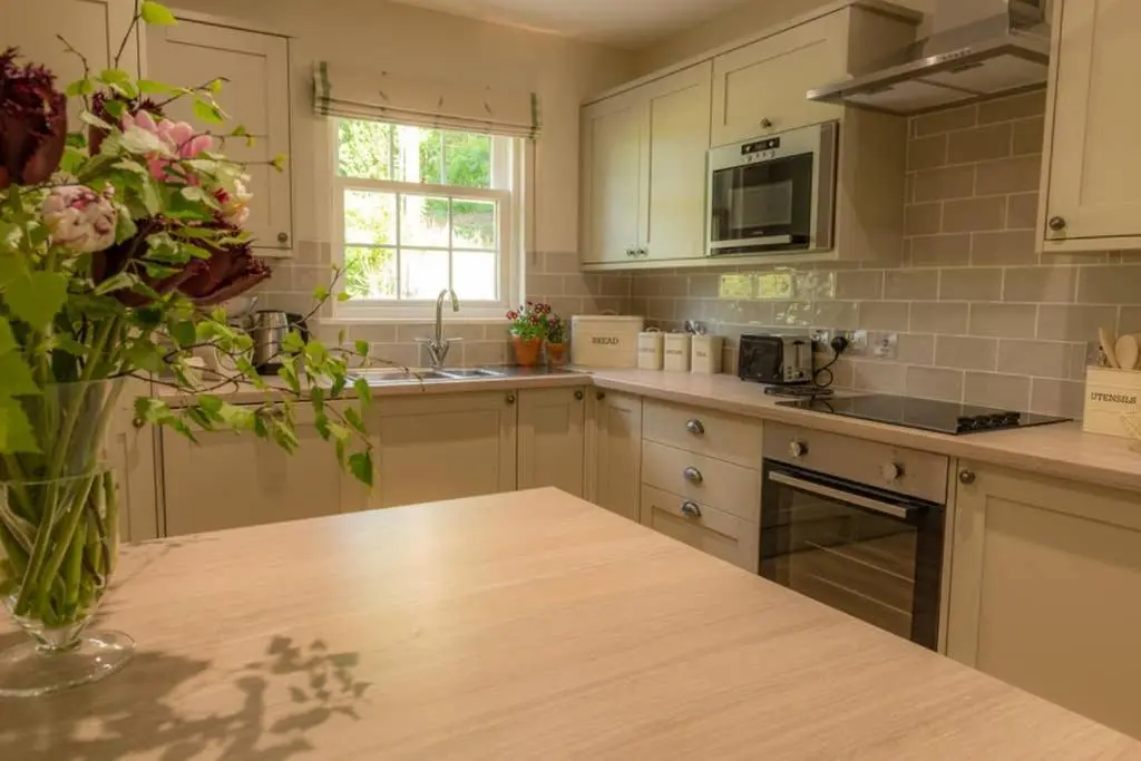 a kitchen with white cabinets and a table with a vase of flowers at Quarry Gardens Lodge in Fochabers