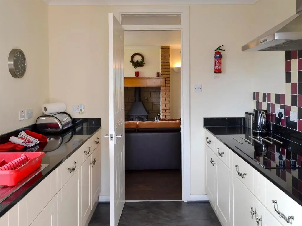 a kitchen with white cabinets and black counter tops at Holly Lodge in Aviemore