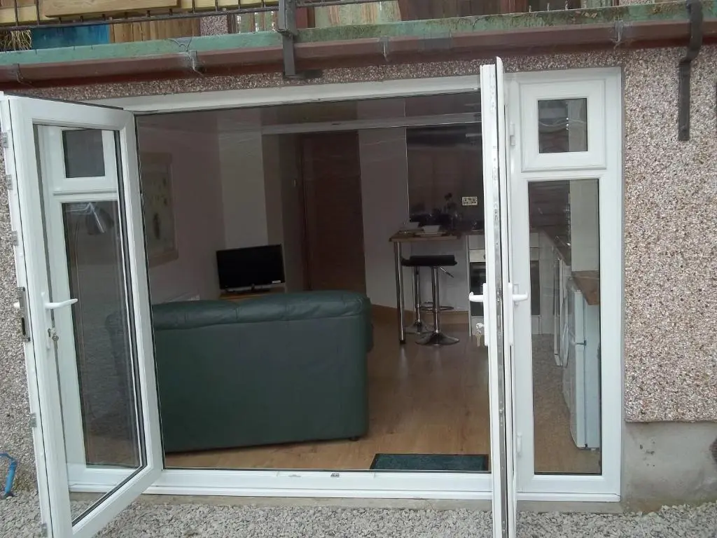 a sliding glass door with a couch in a room at The Wee Thistle Loch Ness in Drumnadrochit