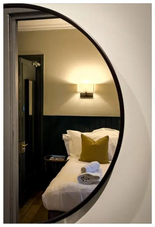 a mirror reflecting a bed with white sheets and green pillows at The Balavoulin - Pub with Rooms in Aviemore