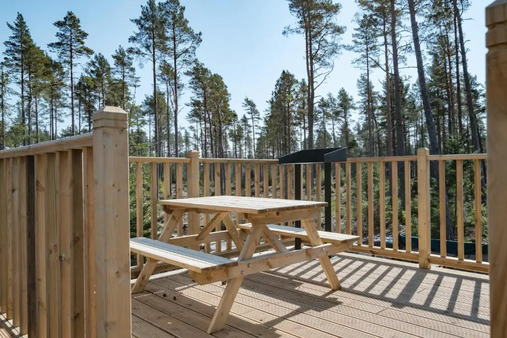 a wooden deck with a picnic table and a grill at Cairngorm Bothies in Aboyne