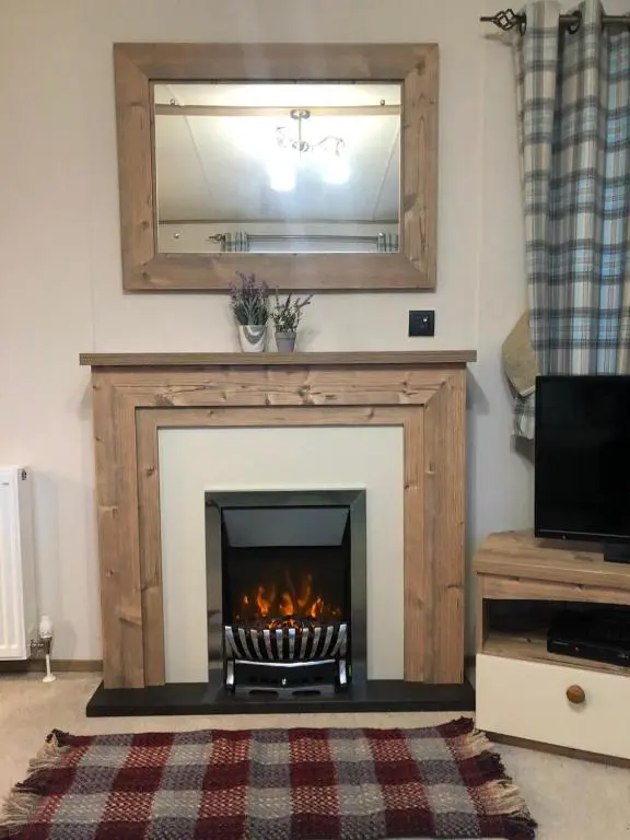 a living room with a fireplace and a mirror at 81 The Heathers, Aviemore Holiday Park , Dalfaber rd Aviemore PH22 1PX in Aviemore
