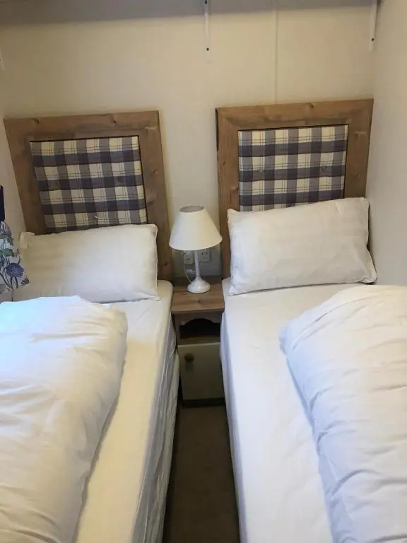 two beds in a room with a table with a lamp at 81 The Heathers, Aviemore Holiday Park , Dalfaber rd Aviemore PH22 1PX in Aviemore