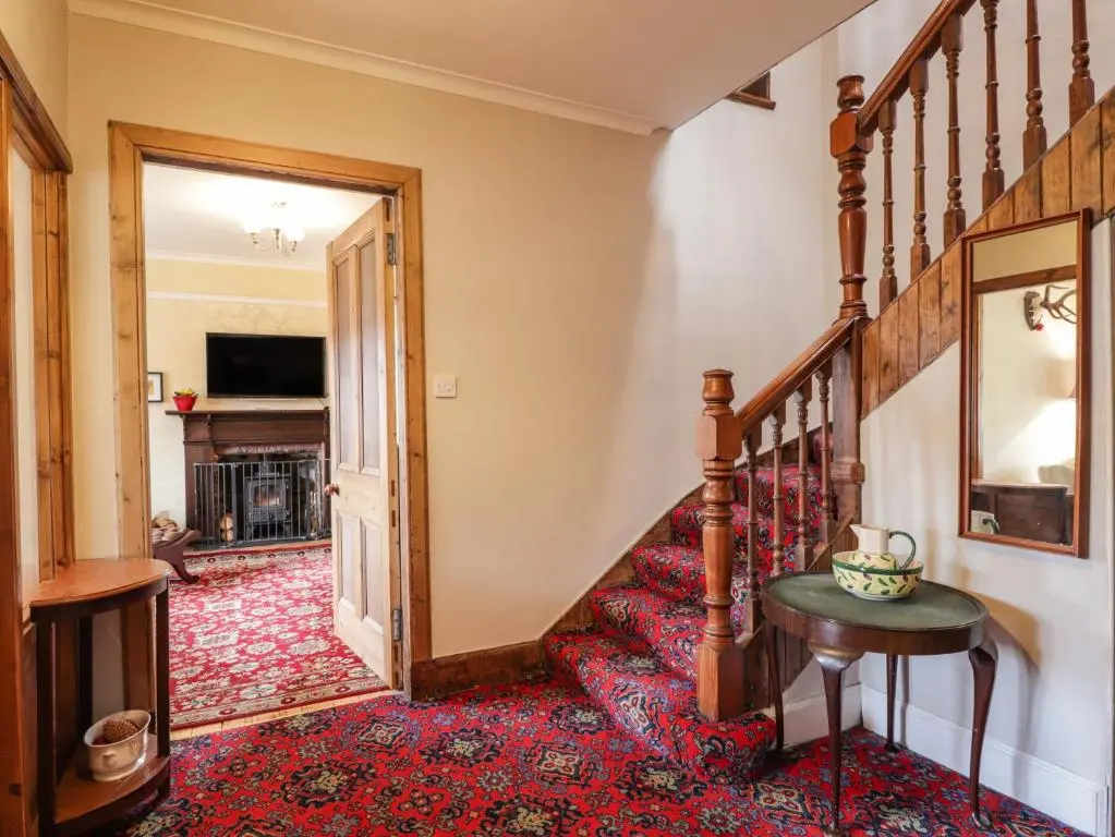 a hallway with a staircase with a table and a television at Glencanisp in Aviemore