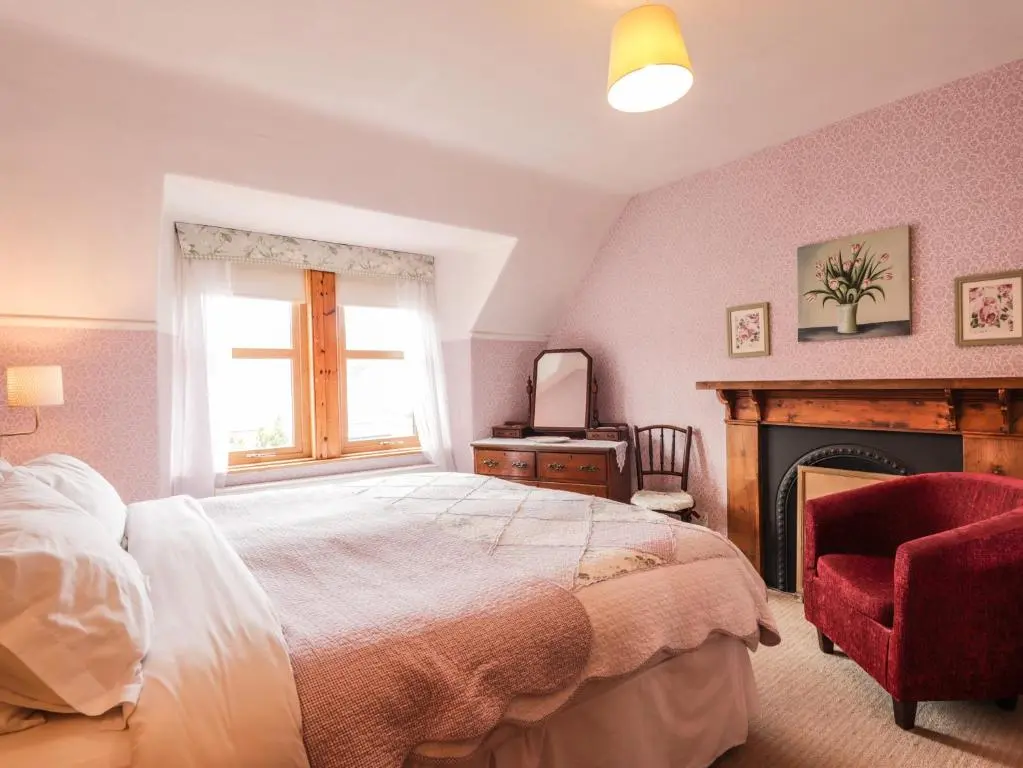 a bedroom with a bed and a fireplace and a window at Glencanisp in Aviemore