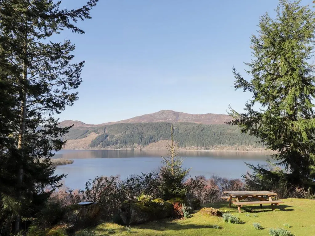 a picnic table and a lake with mountains in the background at Faodail Glenlia in Foyers