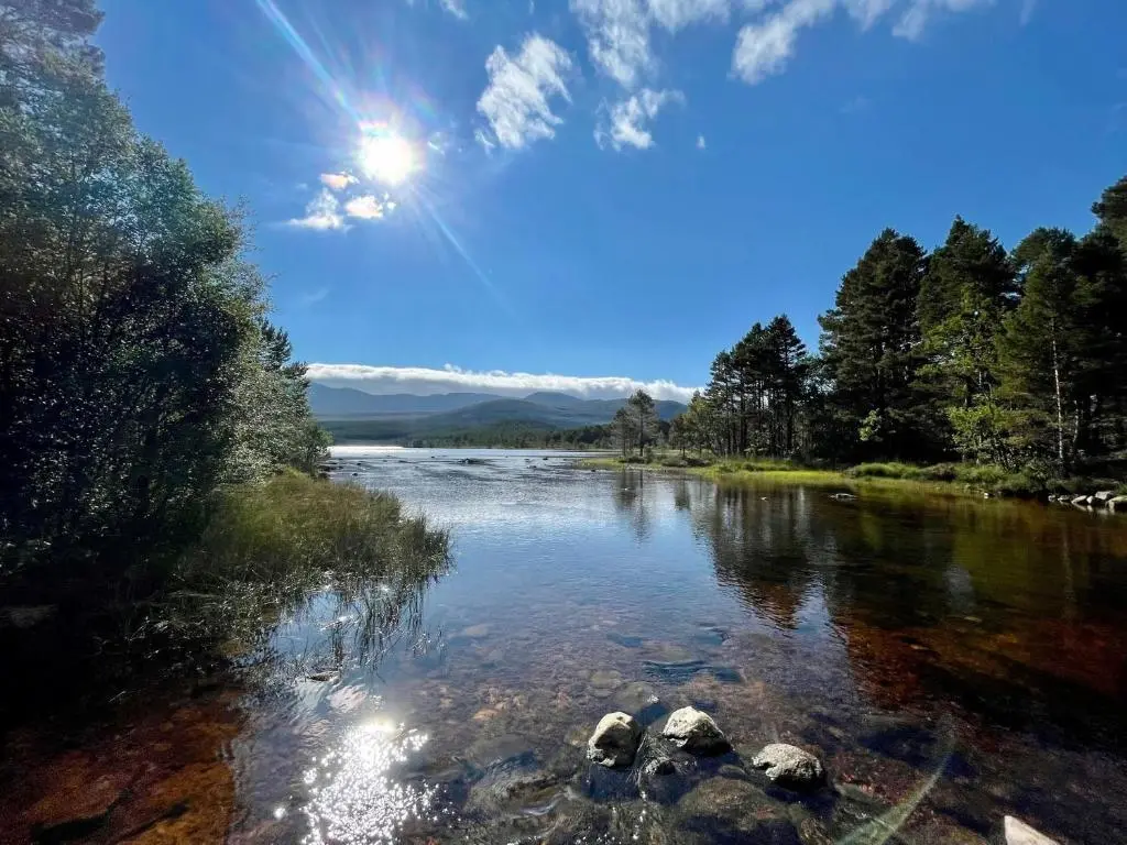a river with rocks and the sun in the sky at Wildcat Lodge in Kingussie