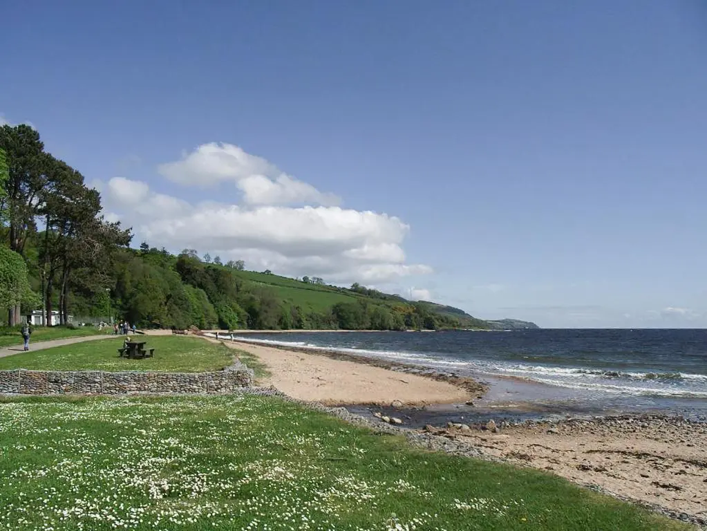 a beach with people sitting on a bench next to the water at Heather Lodge in Glenurguhart