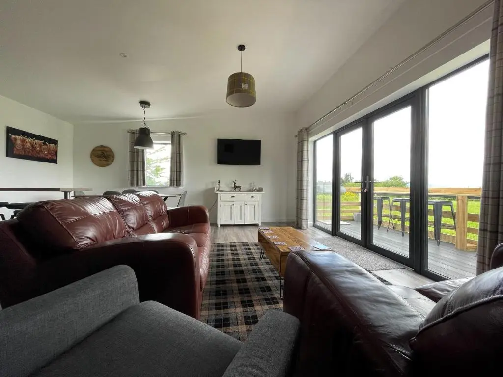 a living room with leather furniture and a large window at Willow Lodge in Muir of Ord