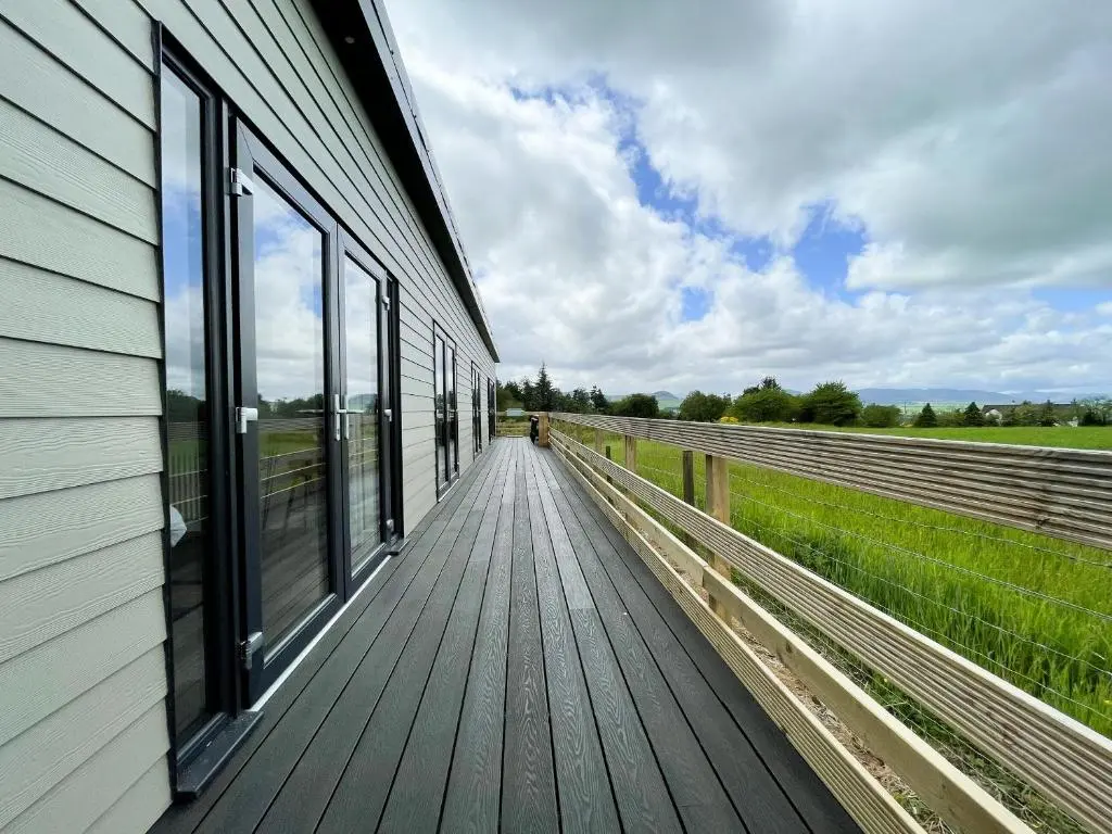 a wooden walkway next to a building with windows at Willow Lodge in Muir of Ord