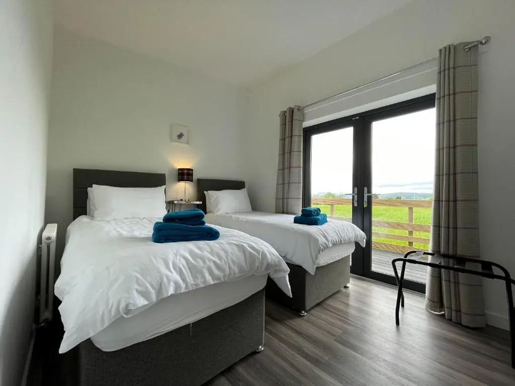 two beds in a room with a large window at Willow Lodge in Muir of Ord