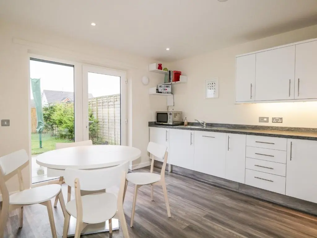 a kitchen with white cabinets and a table and chairs at Skoglendi in Boat of Garten