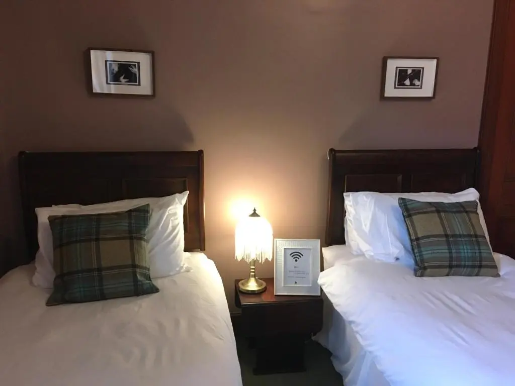two beds in a room with a lamp on a table at Brooklynn Guest House in Grantown on Spey