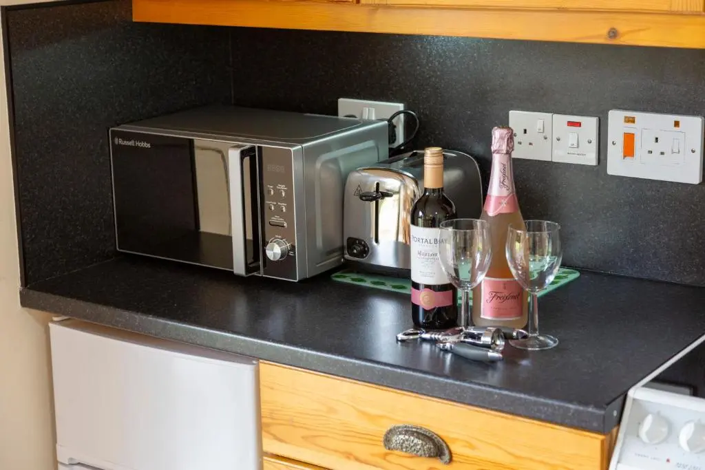 a kitchen counter with a microwave and wine bottles and glasses at Scandinavian Village Ltd in Aviemore