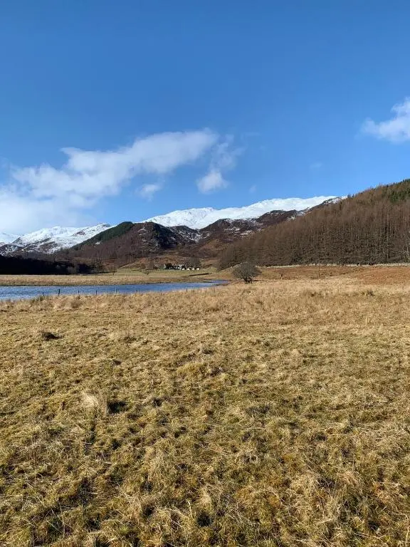 a field with a lake and snow covered mountains at Craskie Glamping Pods in Inverness