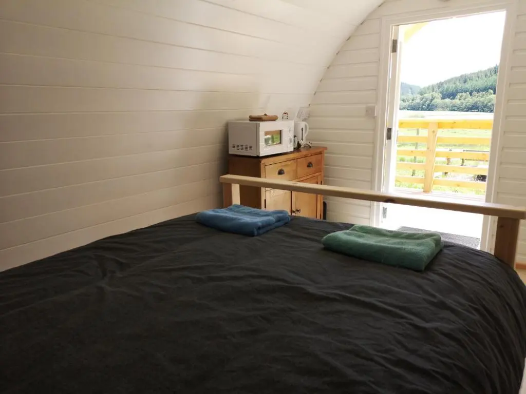 a bedroom with a bed with a microwave and a window at Craskie Glamping Pods in Inverness