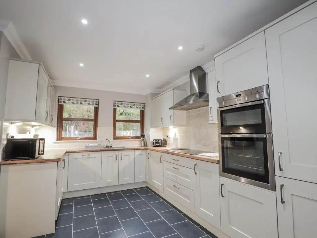 a kitchen with white cabinets and black appliances at Burnside House in Aviemore