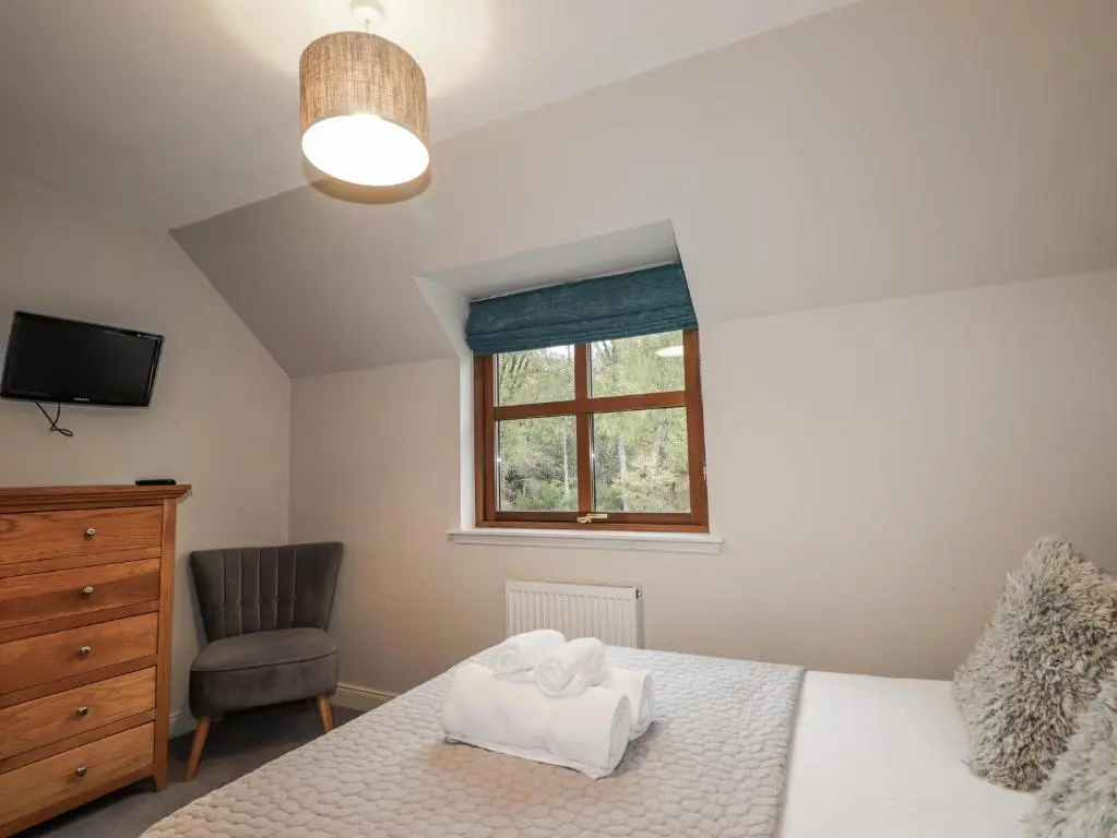 a bedroom with a bed and a chair and a window at Burnside House in Aviemore