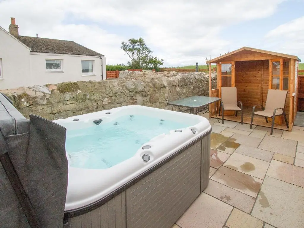 a hot tub on a patio next to a building at Grieve's Cottage in Portmahomack