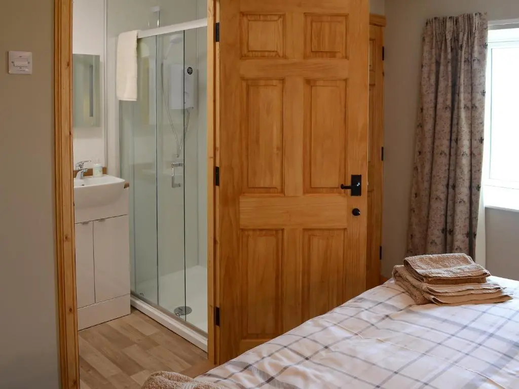 a bedroom with a wooden door and a shower at Grieve's Cottage in Portmahomack