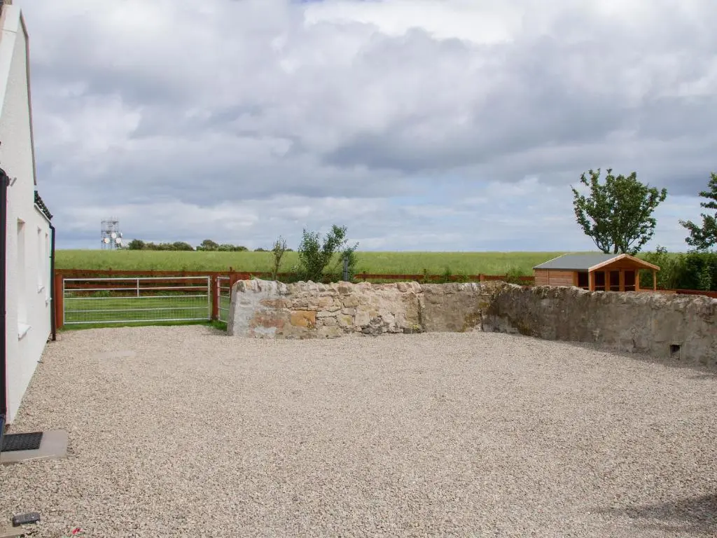 a stone wall next to a fence and a field at Grieve's Cottage in Portmahomack