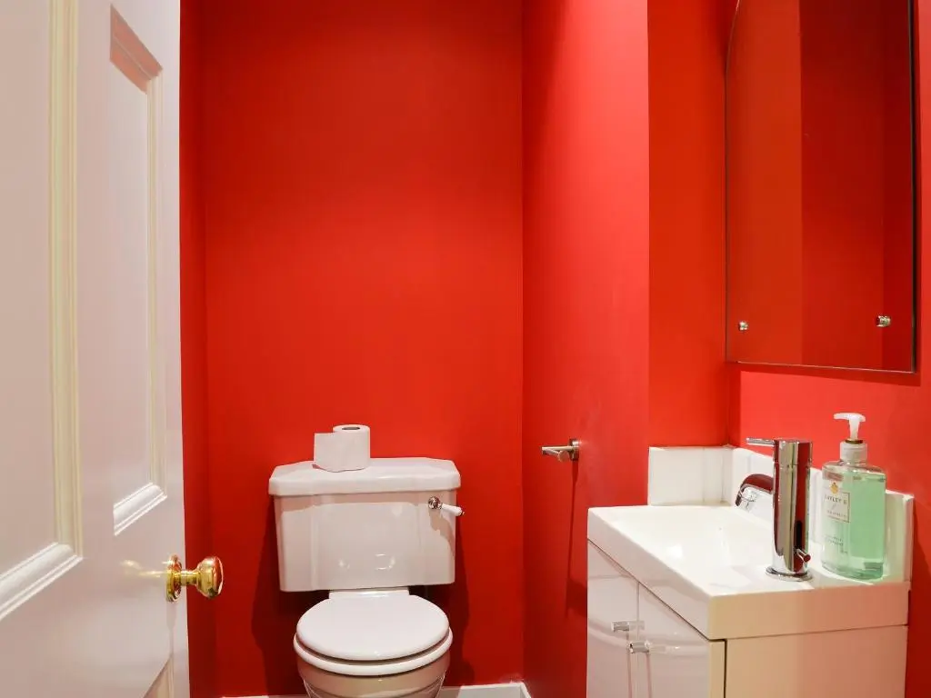 a red bathroom with a toilet and a sink at Dairy Cottage in Whitehouse