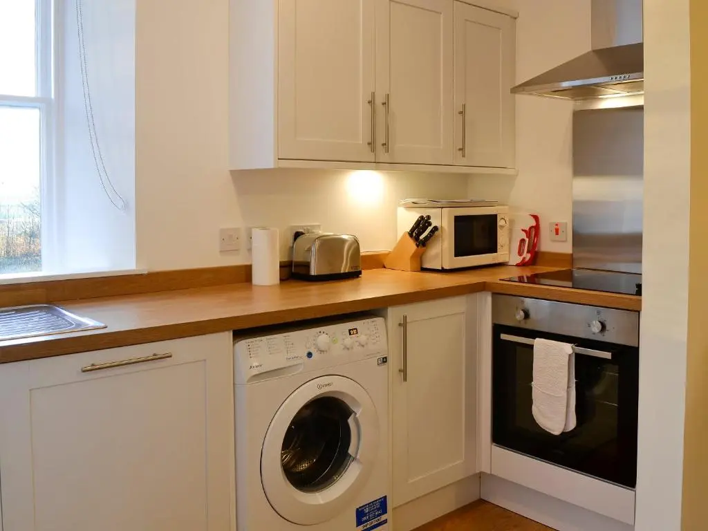 a kitchen with a washing machine and a microwave at Dairy Cottage in Whitehouse