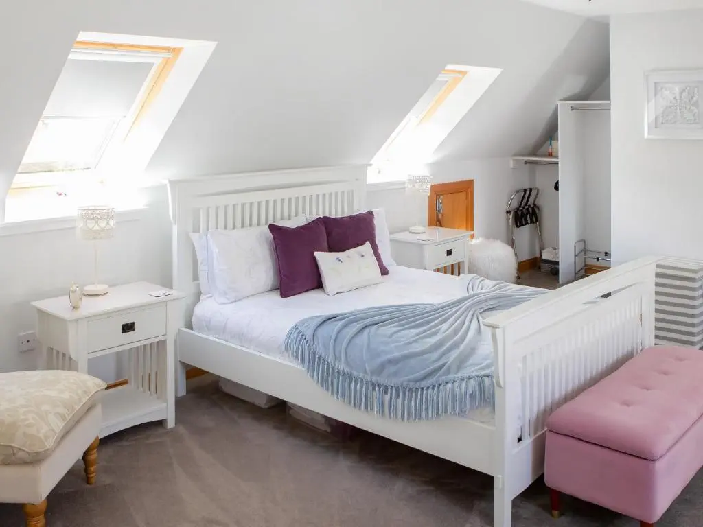 a bedroom with a white bed and two windows at Rose Cottage in Dingwall