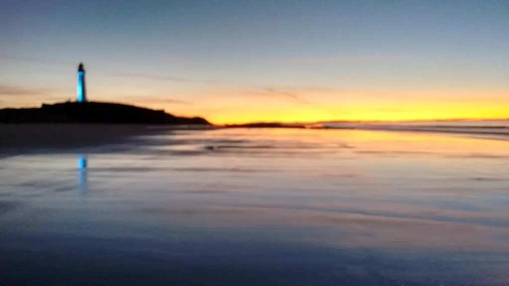 a view of a beach with a lighthouse at sunset at Taid's Retreat Silversands Cove beach lossiemouth in Lossiemouth