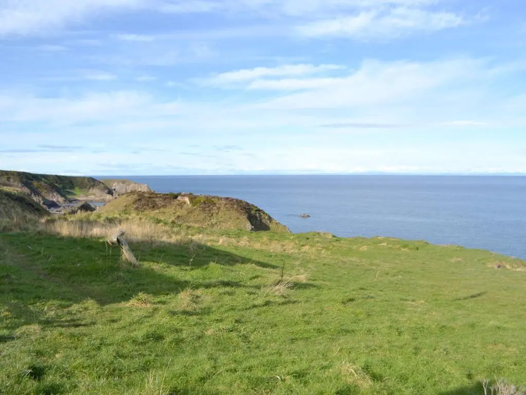 a grassy hill with the ocean in the background at Seabreezes - Uk30690 in Portknockie