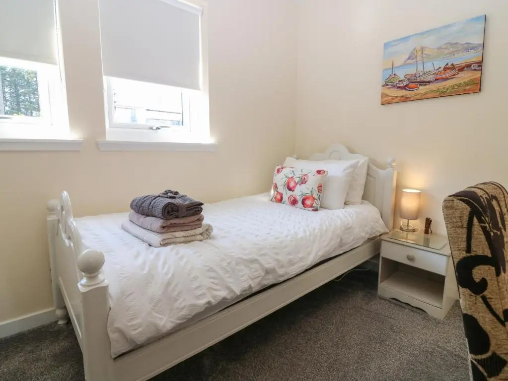 a small white bed in a room with two windows at Berg Cottage in Ballindalloch