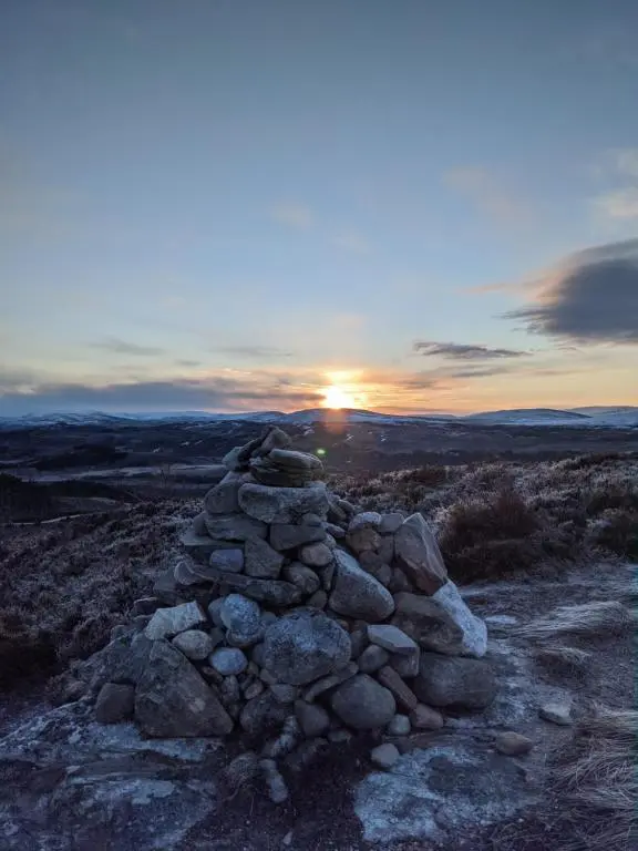 a stack of rocks on top of a hill with the sunset at Wee Wilds in Newtonmore