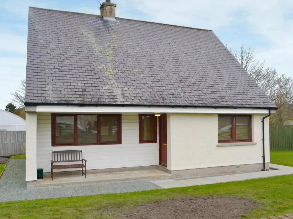 a small white house with a bench in a yard at Cluaran Cottage in Tain