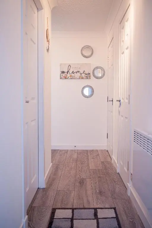 a hallway with white walls and wooden floors and white doors at Millburn Apartment in Inverness