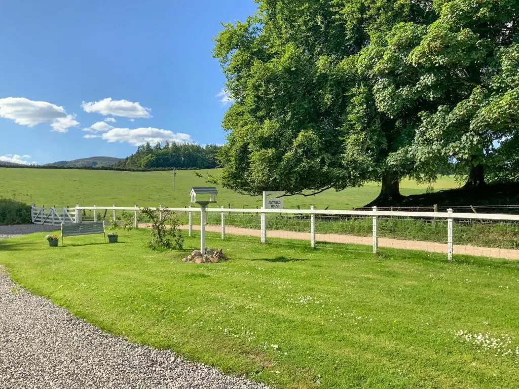 a white fence next to a field with a tree at Antfield House in Lochend