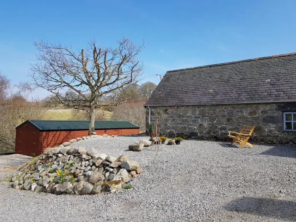 a stone building with a pile of rocks next to a tree at Jakels Rest in Lairg