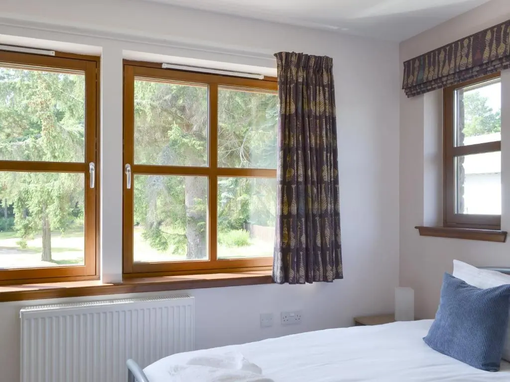 a bedroom with two windows and a white bed at Battanropie Lodge in Carrbridge