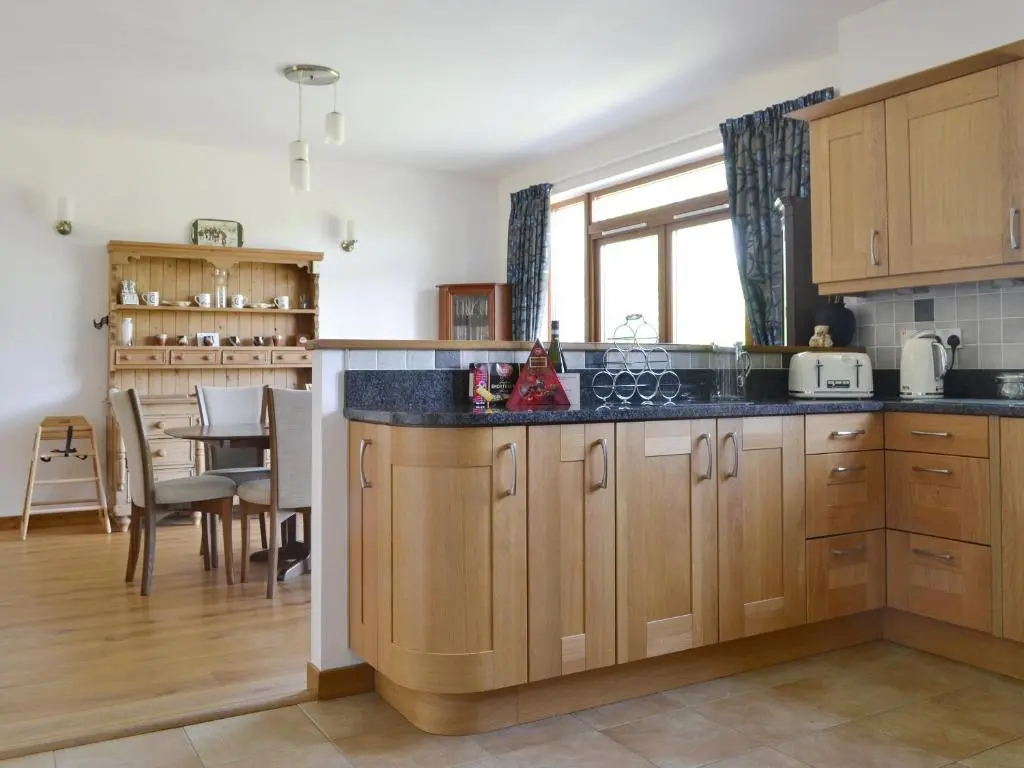 a kitchen with wooden cabinets and a dining room at Battanropie Lodge in Carrbridge