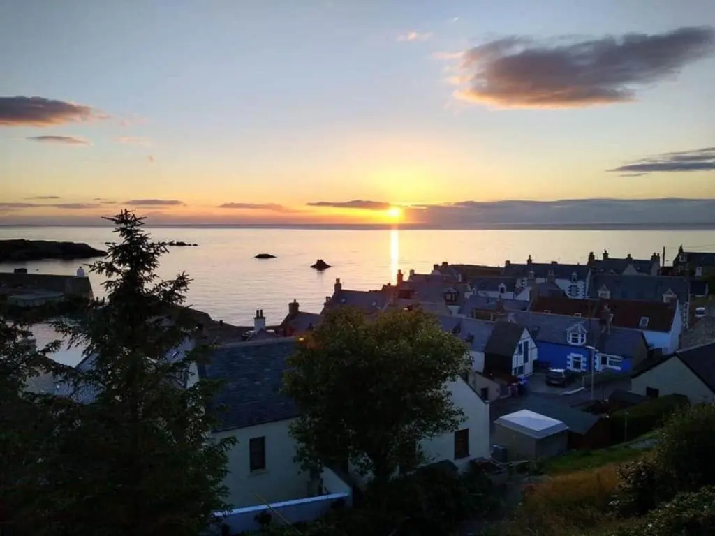 a city with the sun setting over the water at The View 3-Bed Cottage Findochty Buckie Moray in Findochty