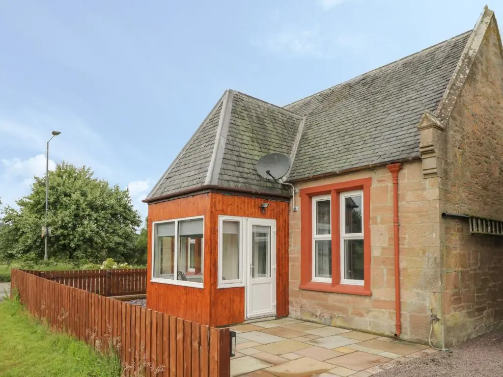 a small brick house with a white door at Blantyre Cottage in Muir of Ord