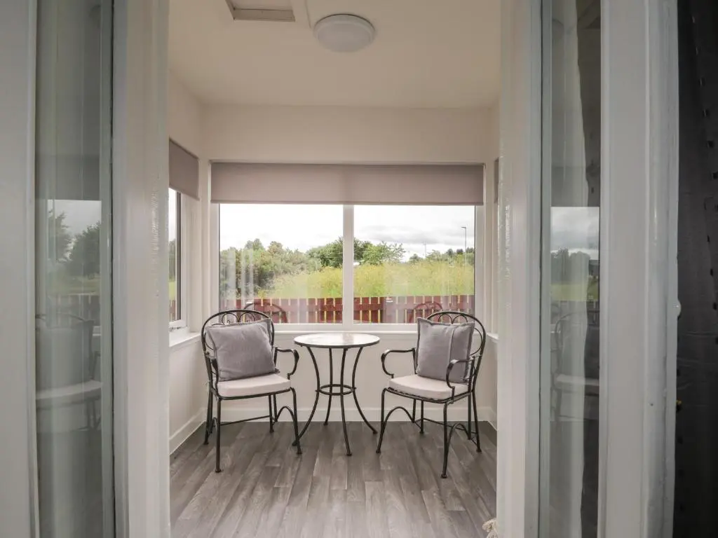 a balcony with two chairs and a table and a window at Blantyre Cottage in Muir of Ord