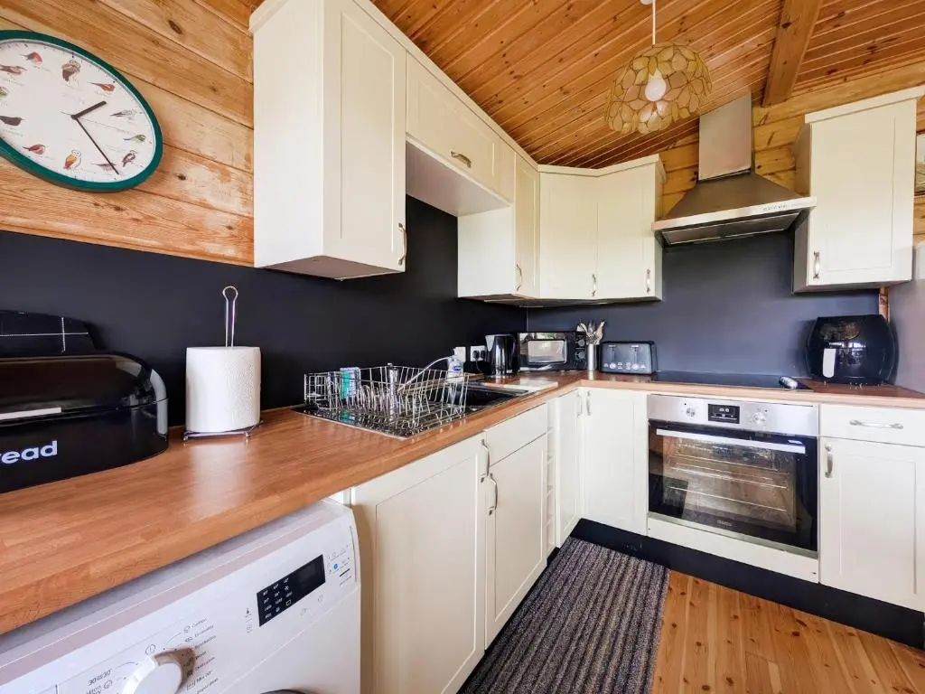 a kitchen with white cabinets and a clock on the wall at Red Kite Cottage in Tore