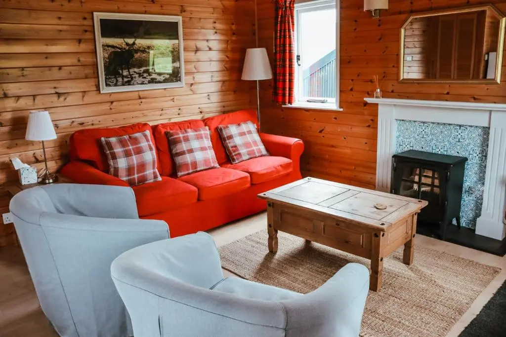 a living room with a red couch and two chairs at Cabins at Old Pier House in Fort Augustus
