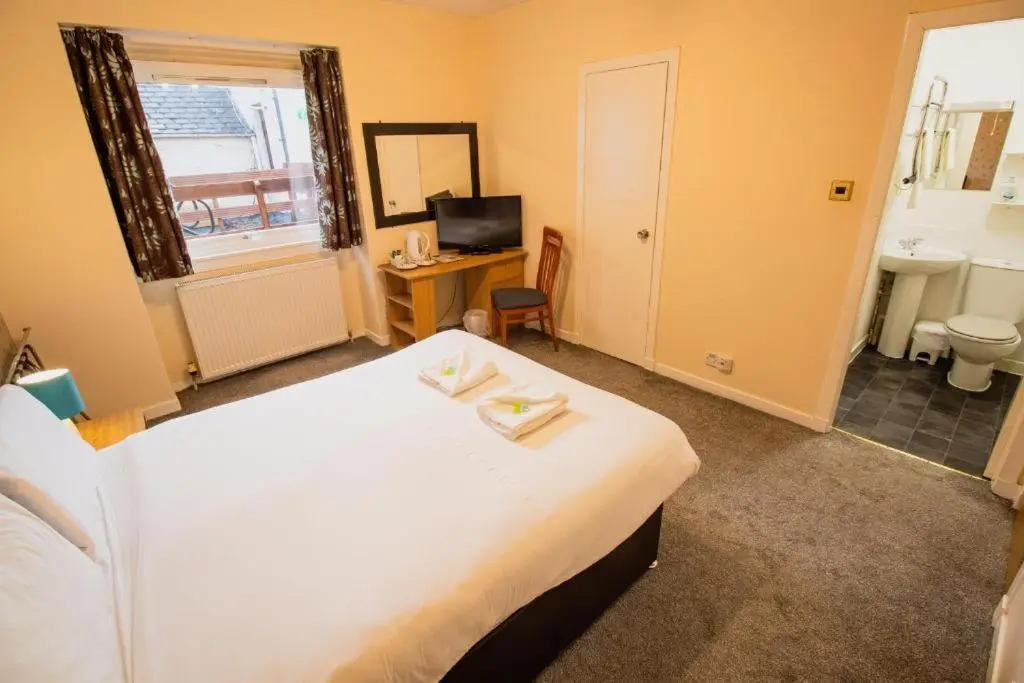 a bedroom with a bed and a bathroom with a sink at The Ben Mhor Hotel, Bar & Restaurant in Grantown on Spey